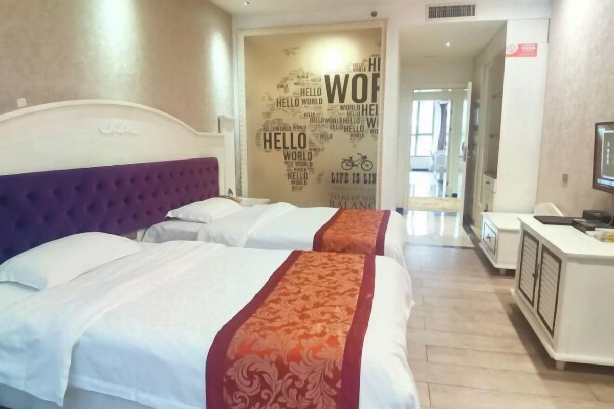 A hotel room with two beds, a headboard, a desk with a chair, and a wall with motivational words.