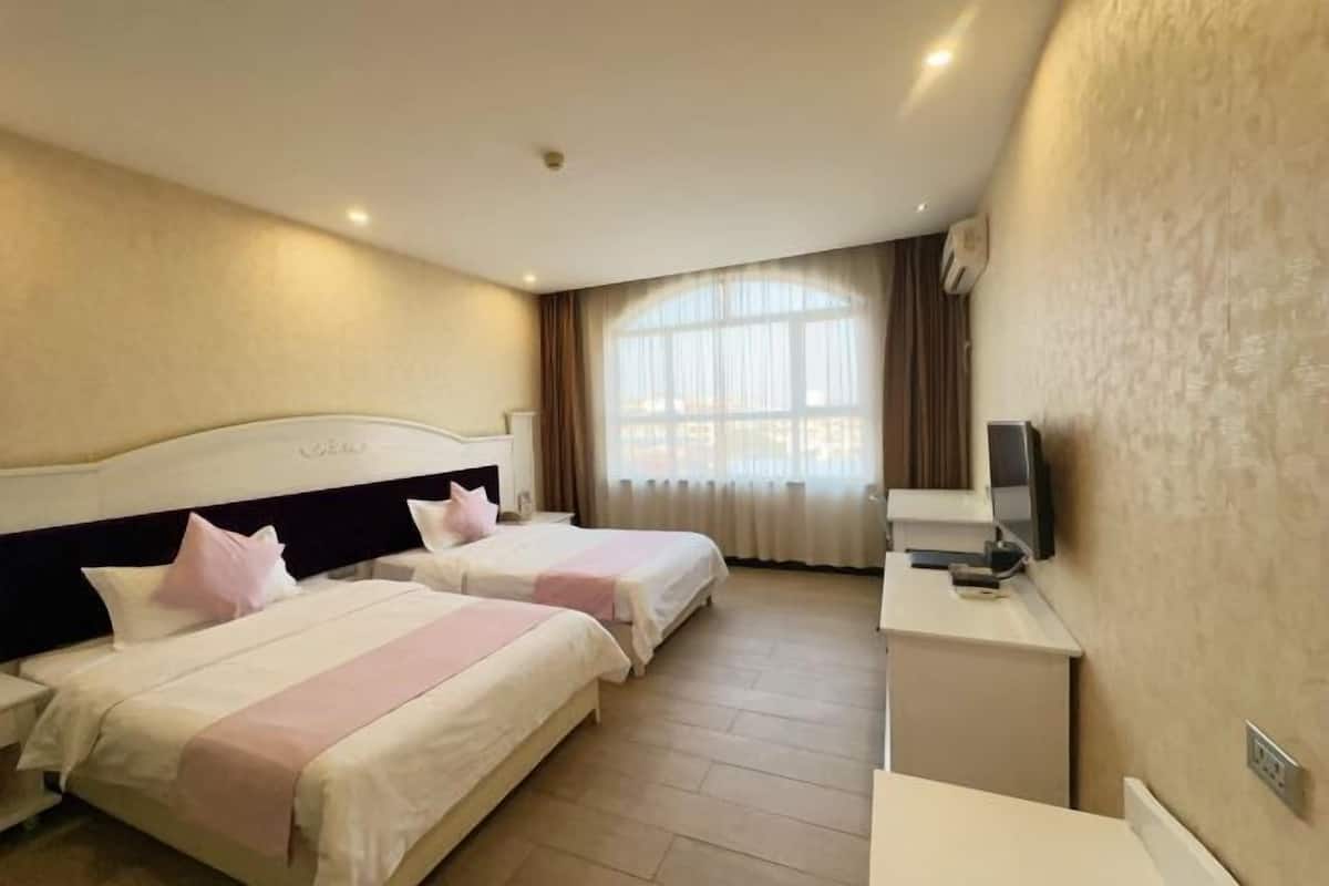 A hotel room with two beds, a desk, a TV, and a large window with curtains.