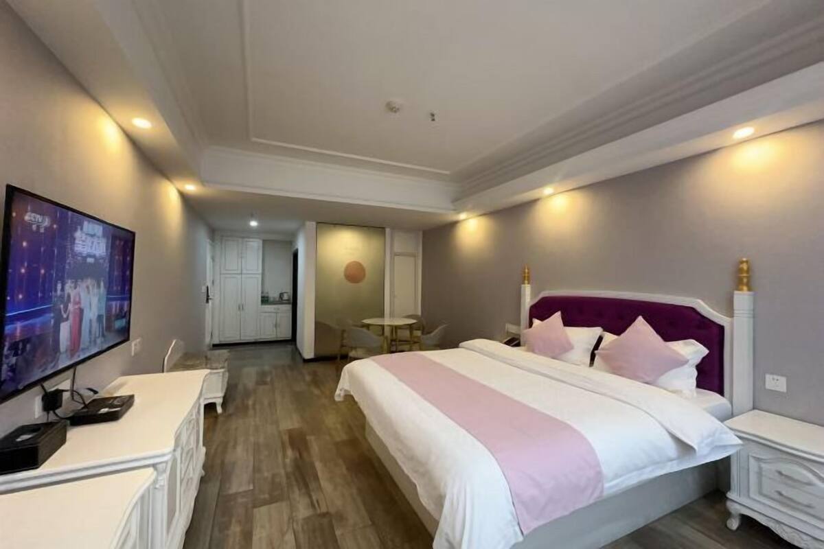 A hotel room with a bed, a desk, a TV, and a bathroom visible in the background.