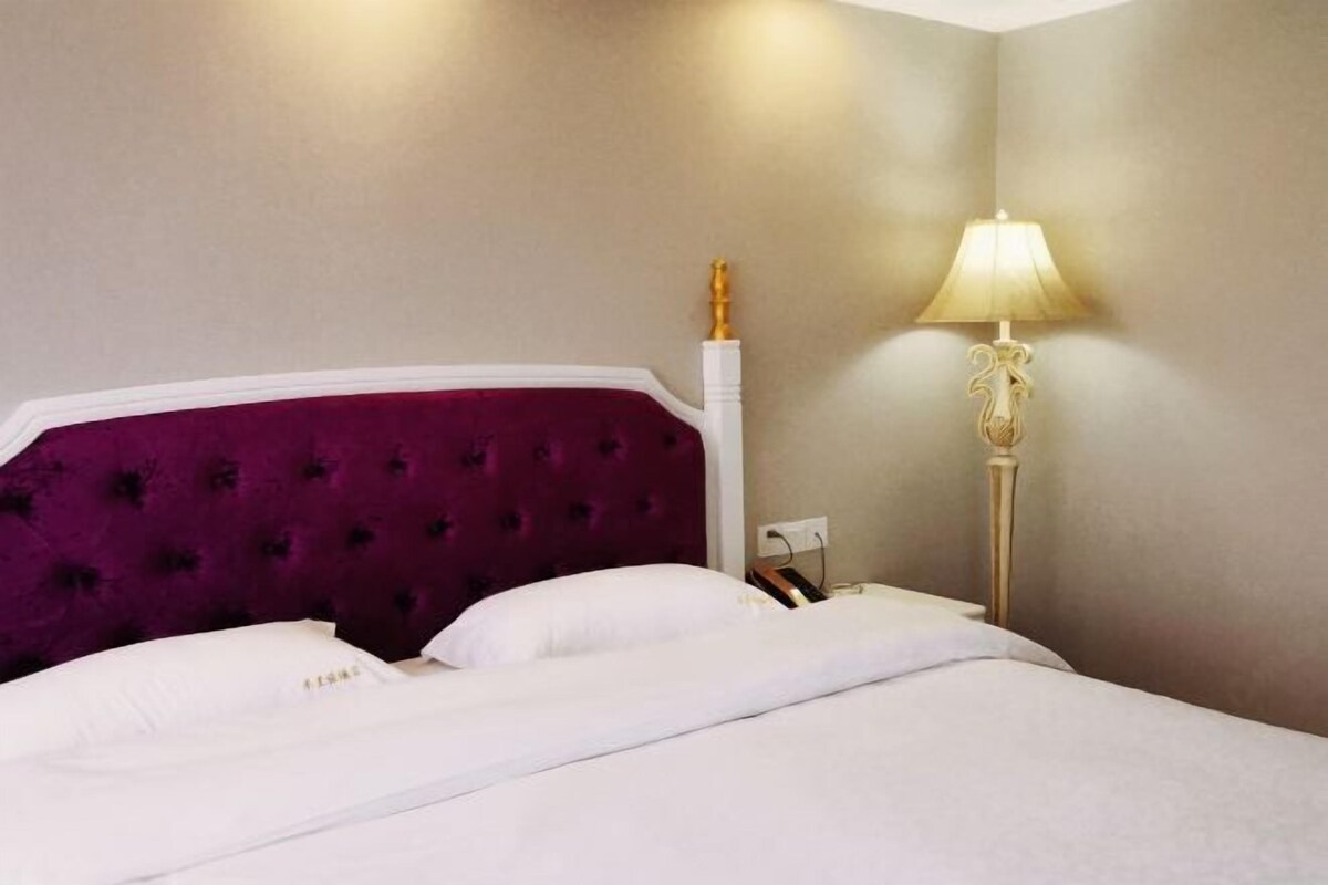 A hotel room with a bed, a headboard, a bedside lamp, and a wall socket.