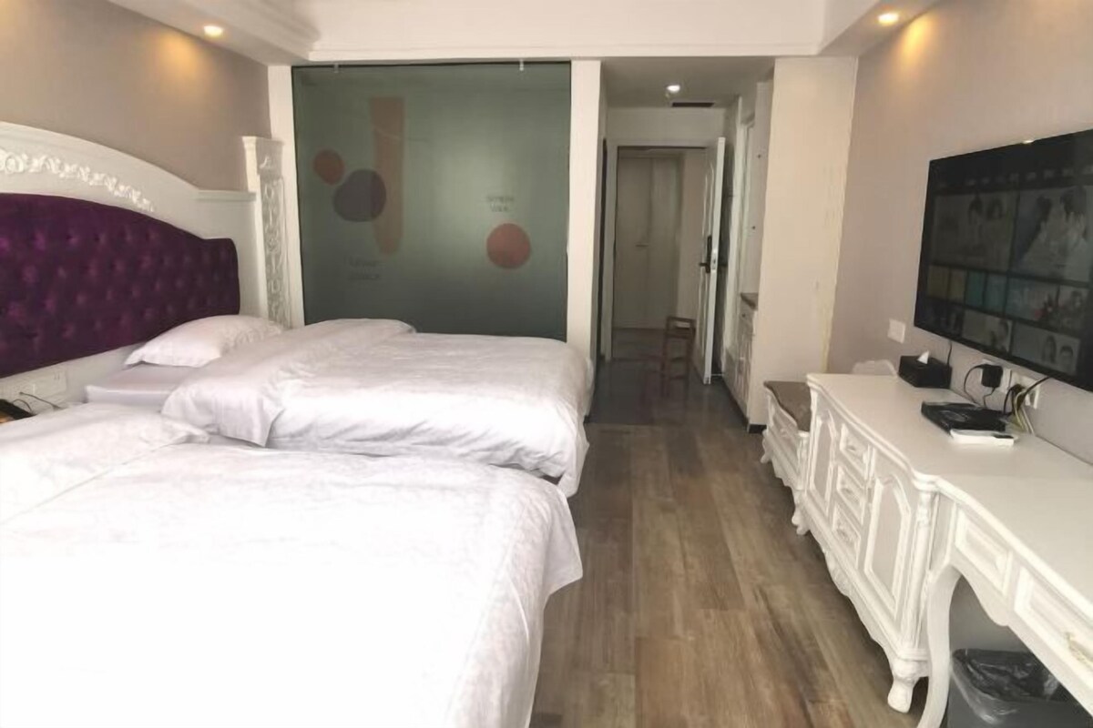 A hotel room with two beds, a white dresser, and a large TV on the wall.