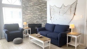 A living room with a stone wall, a blue sofa, a white coffee table, and two lamps. - Third floor condo with ocean views  (Corpus Christi)