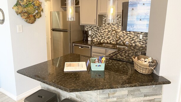 A modern kitchen with granite countertops, stainless steel appliances, and a backsplash with a mosaic tile pattern. - Third floor condo with ocean views  (Corpus Christi)