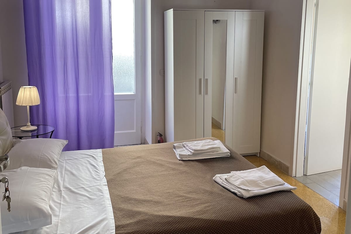Een hotelkamer met een bed, een kledingkast, een lamp en een raam met paarse gordijnen.