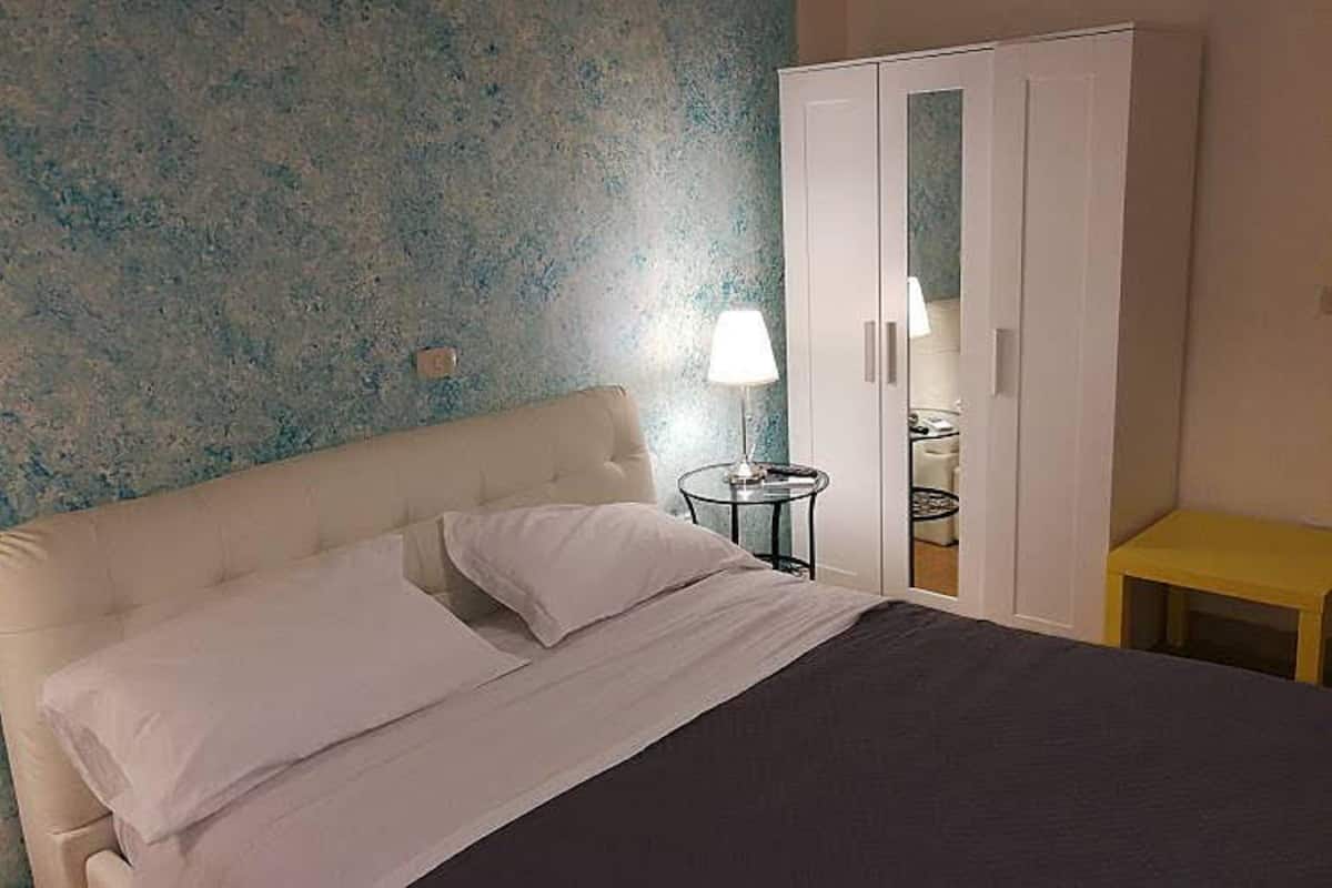 Een slaapkamer met een bed, nachtkastje, lamp en een kledingkast.
