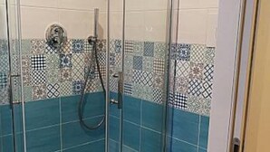 A shower with glass doors, a toilet, and a tiled wall with a pattern. - B&B Antichi Riverberi in Station (Salerno)