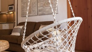 Een macramé hangstoel in een kamer met een houten plafond, een bruine bank en een houten vloer.