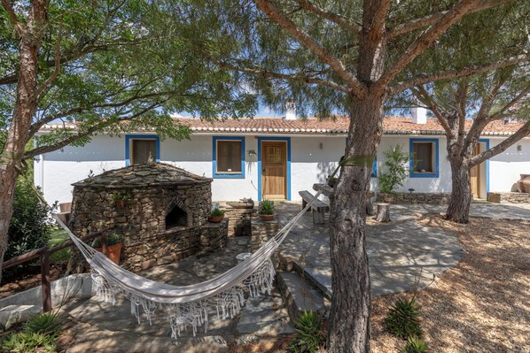 A white building with blue trim, a stone oven, and a hammock.