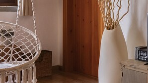 Een kamer met een hangstoel van macramé, een geweven poef, een witte vaas met takken en een houten kast.