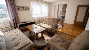 Ein Wohnzimmer mit einer Couch, Sesseln, einem Couchtisch und Blick auf die Küche durch eine offene Tür.