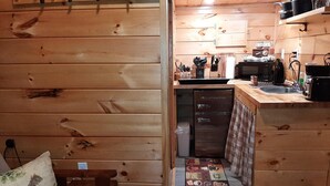 A cozy cabin interior with a wooden interior, a kitchenette with a microwave, toaster, and coffee maker, and a small seating area with a pillow and a bench. - Unique, Cozy Stay near Red River Gorge (Slade)