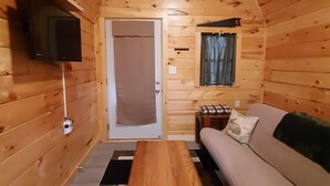 A cozy cabin interior with a wooden ceiling, a sofa, a small table, a television mounted on the wall, and a window with curtains. - Unique, Cozy Stay near Red River Gorge (Slade)