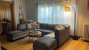 Ein Wohnzimmer mit einem grauen Ecksofa, einem kleinen runden Couchtisch und einer Stehlampe.