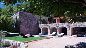 Ein Steingebäude mit Pool, Außenbereich zum Sitzen und überdachtem Bereich.