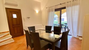 A dining area with a glass table and four chairs, a wooden door, and a window with curtains. - Villas Smeraldas Holiday In Sardinia (Sardegna)