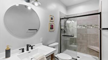 A modern bathroom with a round mirror, white sink, black faucet, and a glass-enclosed shower.