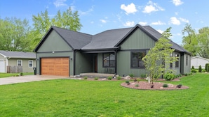Een modern huis met twee verdiepingen, een groene buitenkant, een bruine garage deur en een verzorgd gazon.