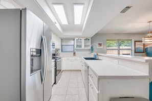 A modern kitchen with white cabinets, a stainless steel refrigerator, and a large island with a sink. - Poolside Golf Paradise: 2 King Bdrms: Beaches 15 Min: Game room: Tee, Sun & Fun (Fort Pierce)
