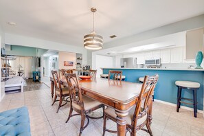 A spacious living area with a dining table surrounded by chairs, a kitchen area with white cabinets and a blue accent wall, and a separate seating area with a blue sofa. - Poolside Golf Paradise: 2 King Bdrms: Beaches 15 Min: Game room: Tee, Sun & Fun (Fort Pierce)