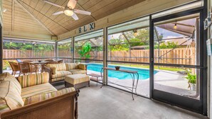 Un patio coperto con mobili in vimini, una ventola a soffitto e vista su una piscina nel giardino.