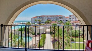 Blick von einem Balkon mit Pool, Palmen und einem Hotel im Hintergrund.