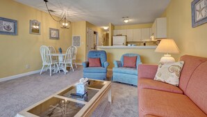 Ein Wohnzimmer mit einem Glastisch, zwei blauen Sesseln, einem roten Sofa und einem Essbereich mit weißen Stühlen.