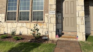 A two-story house with a stone facade, numbered 3305, featuring a central door with a stone archway, multiple windows, and a small front yard with a brick pathway. - Brand new charming 2 bedroom Townhouse get away (Denton)