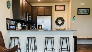A modern kitchen with dark wood cabinets, a stainless steel refrigerator, and a bar area with stools. - Brand new charming 2 bedroom Townhouse get away (Denton)