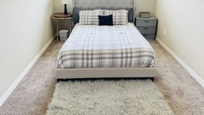 A bedroom with a bed, a nightstand, a lamp, a small plant, and a window. - Brand new charming 2 bedroom Townhouse get away (Denton)