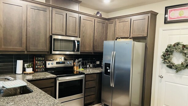 A kitchen with wooden cabinets, stainless steel appliances, granite countertops, and a white door with a wreath. - Brand new charming 2 bedroom Townhouse get away (Denton)
