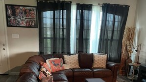 A living room with a brown leather sectional sofa, a small side table, and a floor lamp. - Brand new charming 2 bedroom Townhouse get away (Denton)