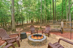 Relax in a serene forest setting with a cozy fire pit surrounded by Adirondack chairs.