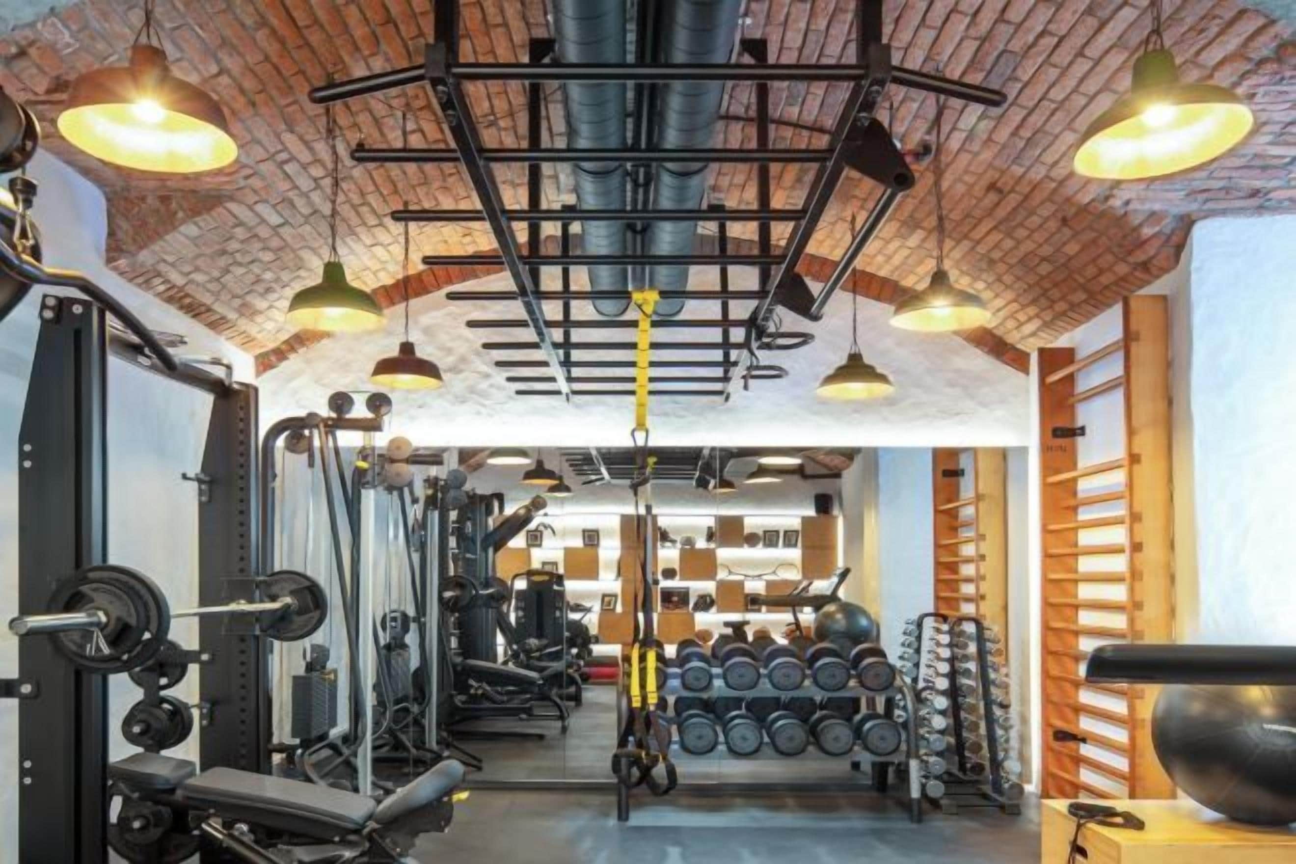Ein Fitnessraum mit Trainingsgeräten, einer Ziegeldecke und Pendelleuchten.