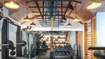 Ein Fitnessraum mit Trainingsgeräten, einer Ziegeldecke und Pendelleuchten.