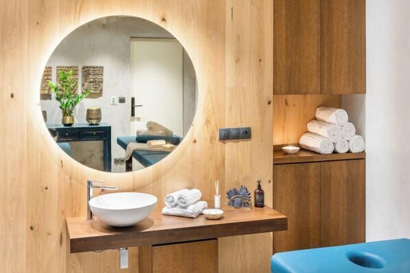 A bathroom with a round mirror, wooden vanity, and a blue bathtub.