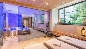 A spa room with a glass wall, a hot tub, and a window with a view of greenery.