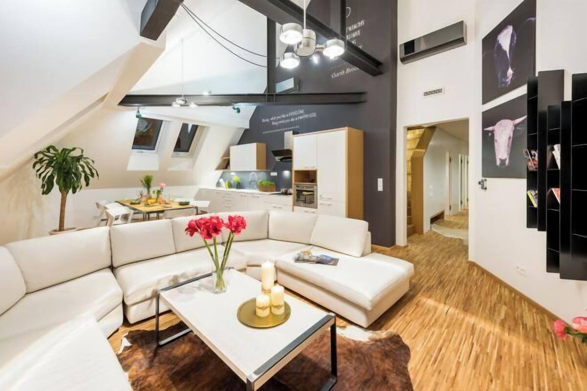 A modern interior with a white sectional sofa, a coffee table with candles, and a dining area with a plant.