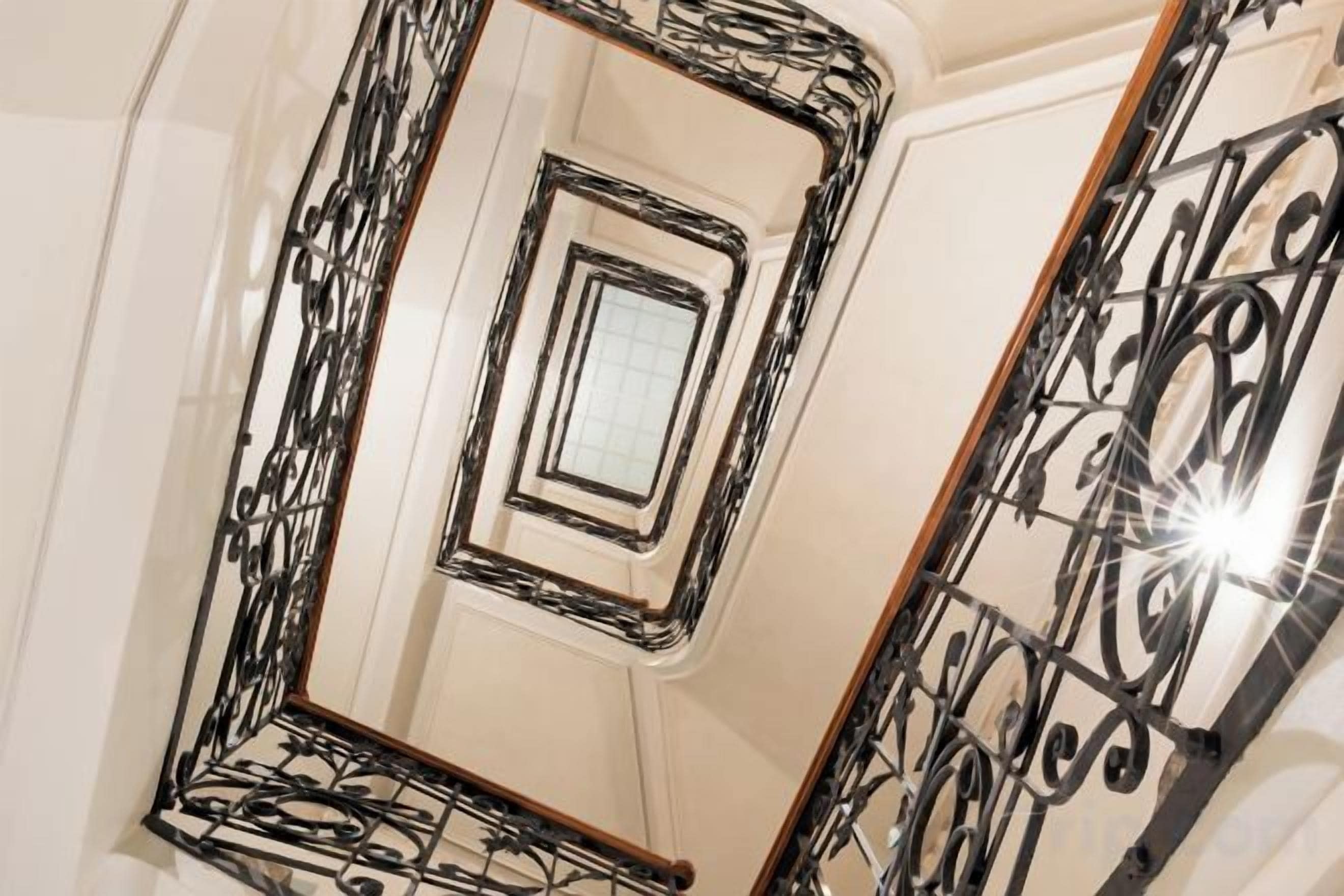 Un escalier en colimaçon orné de rampes en métal ouvragé et d’un mur recouvert de miroirs.