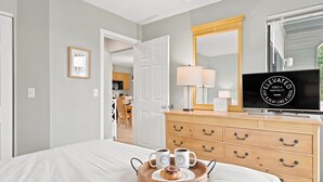 Une chambre d’hôtel équipée d’un lit, d’une télévision, d’une commode et d’un plateau avec des tasses et une pâtisserie.
