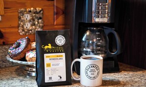 A bag of Panther Coffee Wonderland ground coffee, a white mug with a logo, and a coffee maker on a kitchen counter.