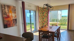 Un coin repas avec une table et des chaises en bois, une grande peinture abstraite au mur et une vue sur l’extérieur grâce à une porte-fenêtre coulissante.