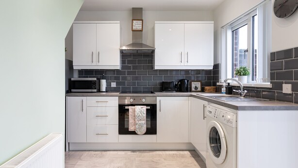 A modern kitchen with white cabinets, a built-in oven, a microwave, and a washing machine.
