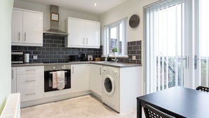 A modern kitchen with white cabinets, a built-in oven, a washing machine, and a window with a view of the outside.