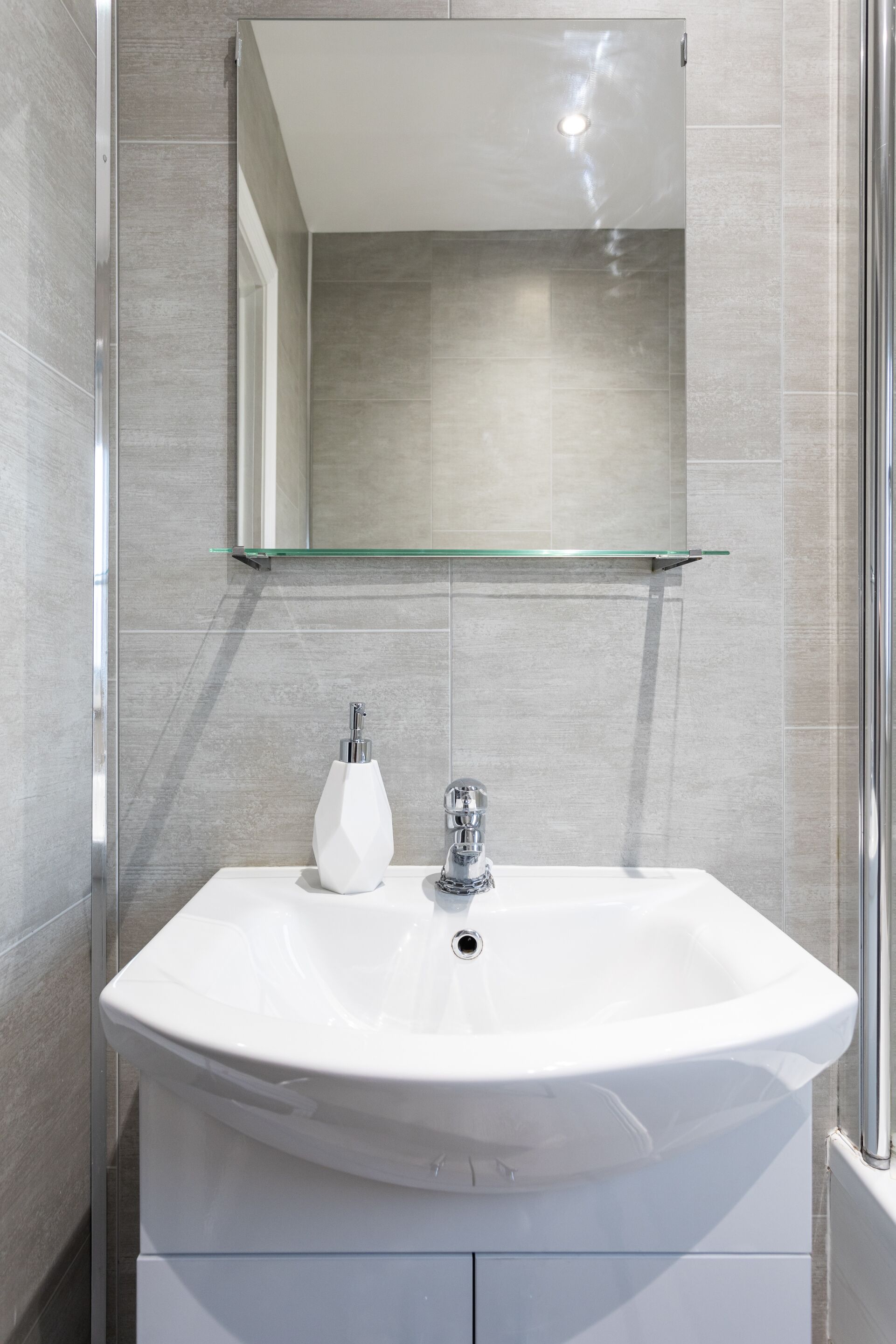 A modern bathroom with a white sink, a glass shelf above it, and a mirror.