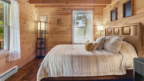 Une chambre à coucher dans un chalet en bois, avec un lit, une table de chevet, une fenêtre avec des rideaux et une étagère fixée au mur.