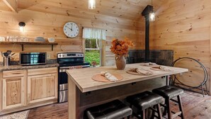 Une cuisine rustique, aménagée dans une cabane en bois, avec un îlot central, un four à micro-ondes, une cuisinière et une horloge au mur.