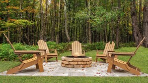 Un foyer extérieur avec deux chaises Adirondack, le tout installé dans un cadre forestier.