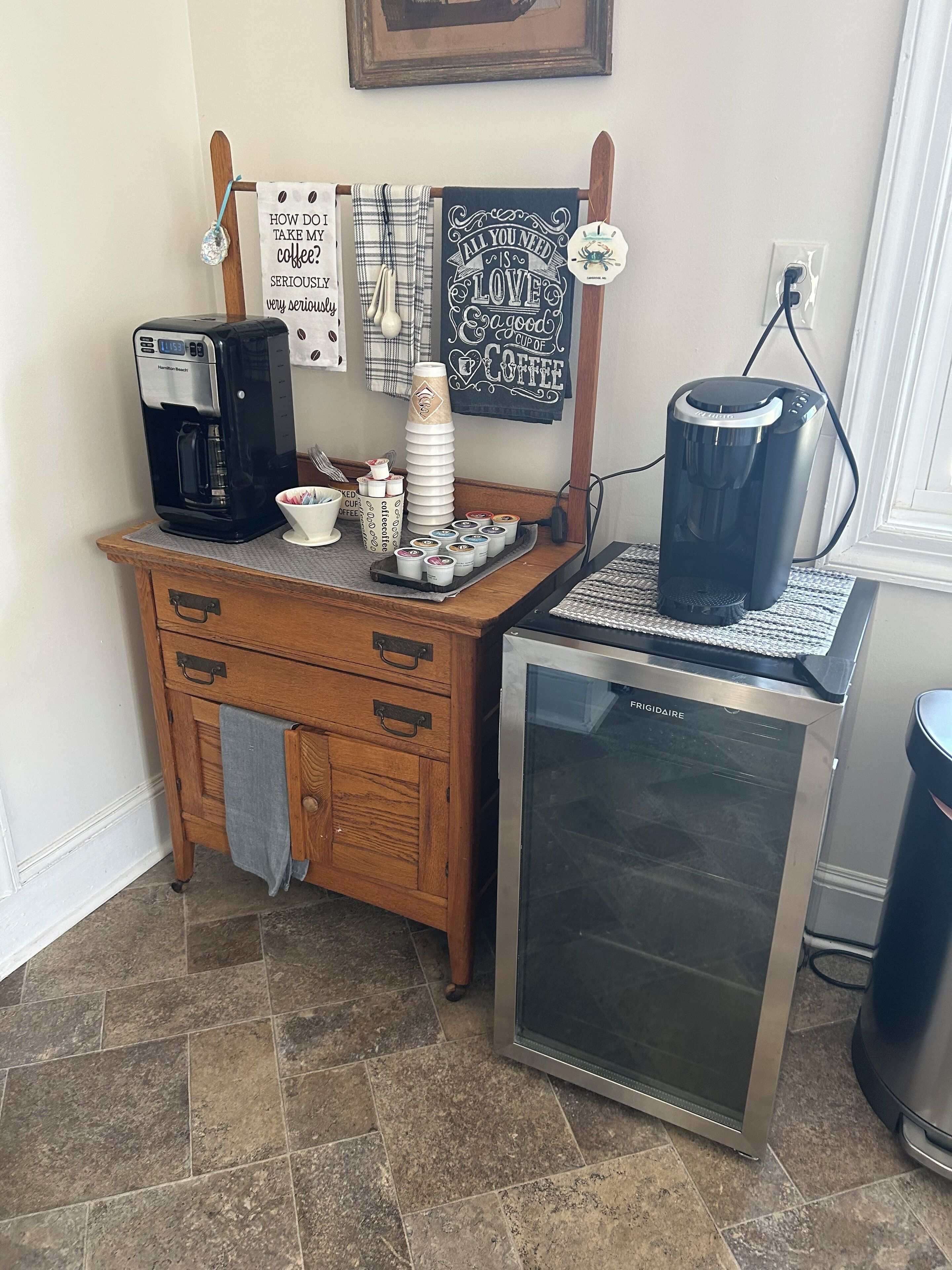 Una zona de cafè amb una màquina de fer cafè Hamilton Beach, un refrigerador Frigidaire i un dispensador de cafè.