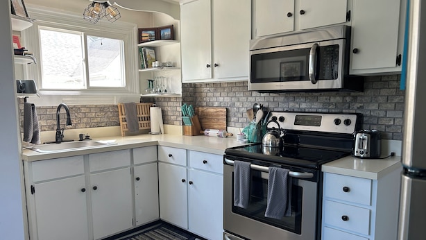 A modern kitchen with white cabinets, a stainless steel stove, a microwave, and a sink. - Sailwinds Loft at Cambridge Creek (Cambridge)