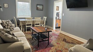 A living room with a beige sofa, a coffee table, and a dining area with a table and chairs. - Sailwinds Loft at Cambridge Creek (Cambridge)